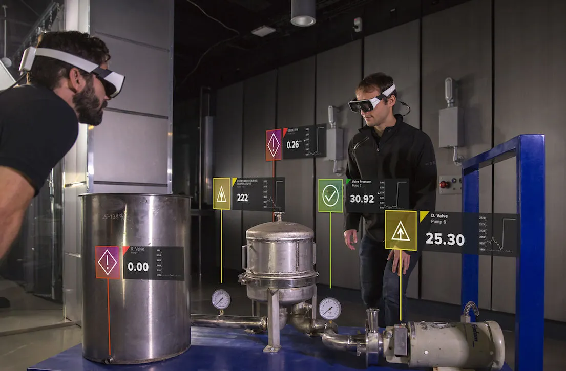 A worker wearing Smart Glasses looking at industrial pipes overlaid with green and red status markers