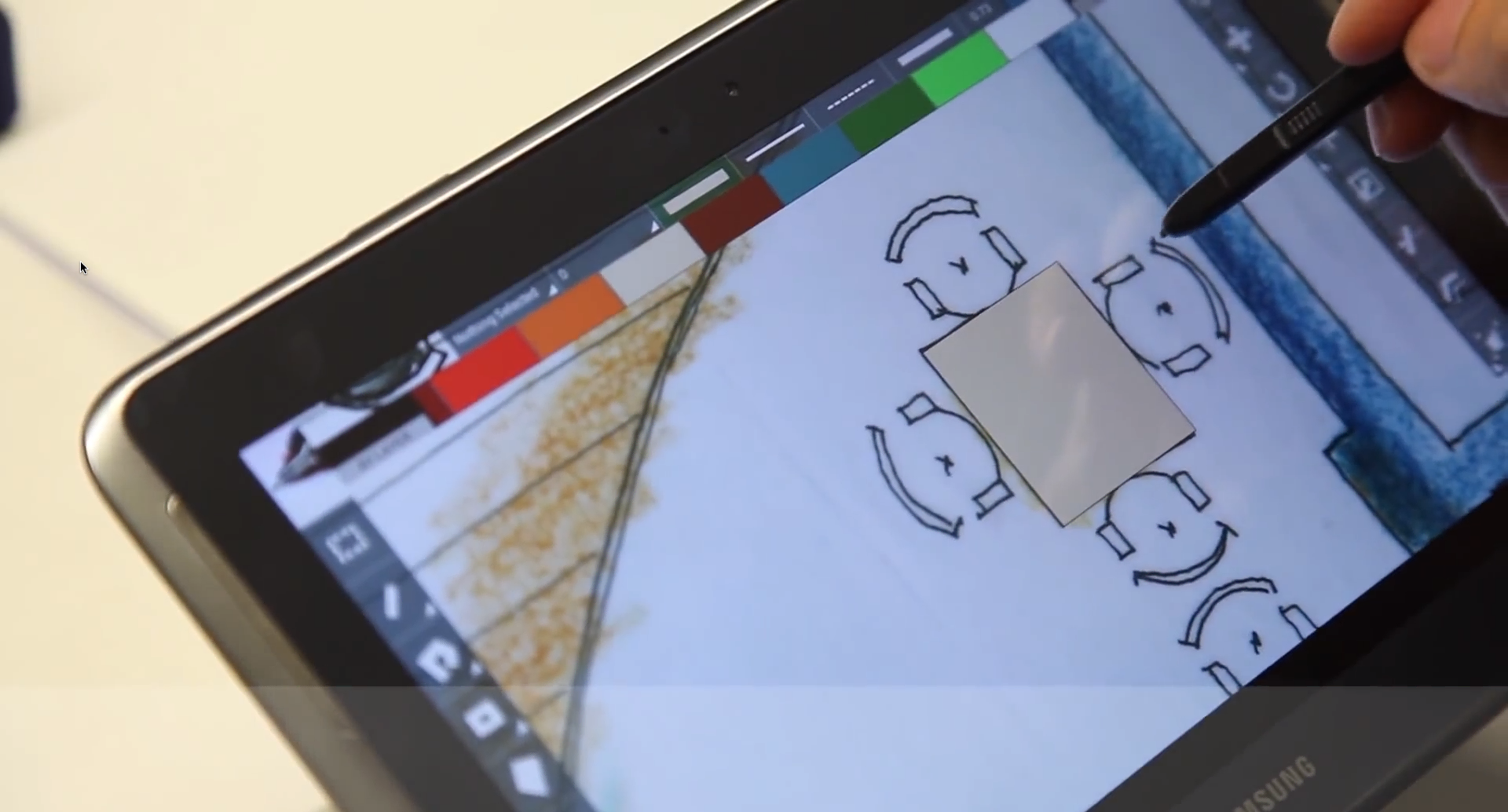A hand drawing on a Samsung tablet with a stylus in CAD Touch, sketching chairs around a table on a floor plan